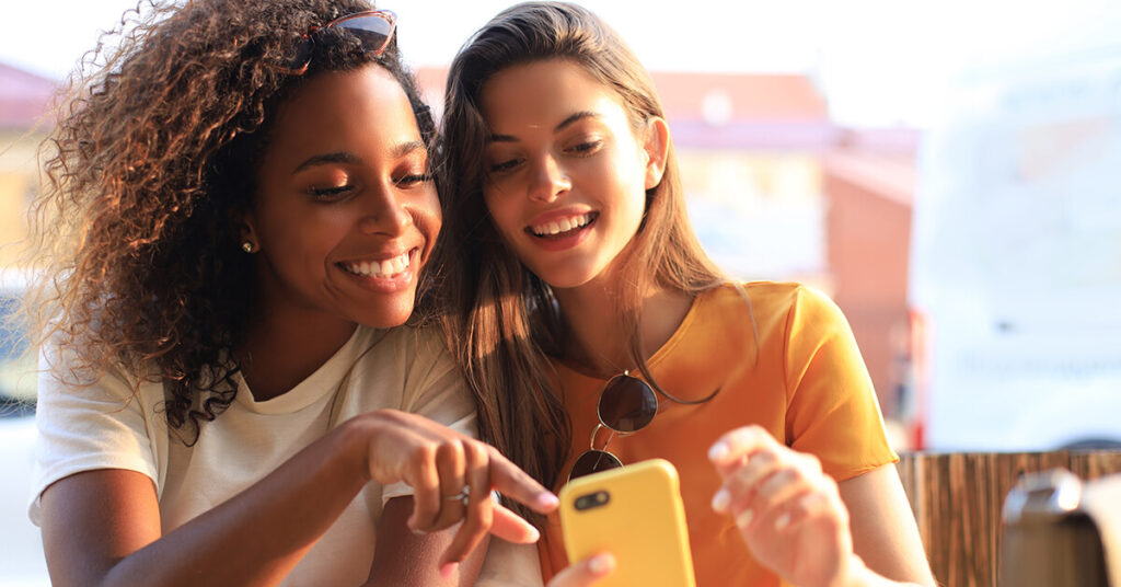 Channel management strategies - two young women smiling, looking at cell phone